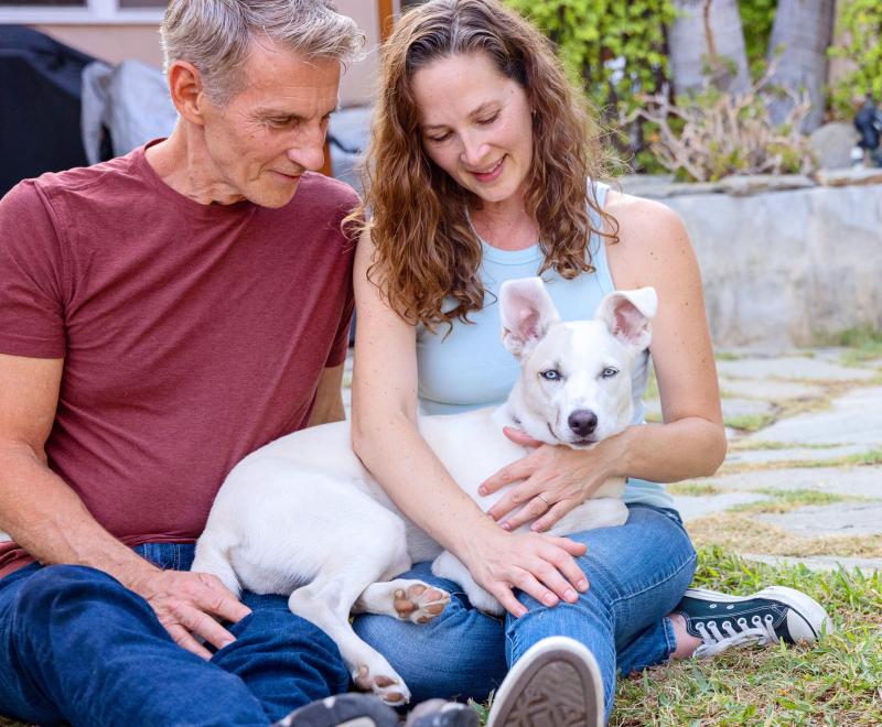 Two smiling people sitting on grass with their dog