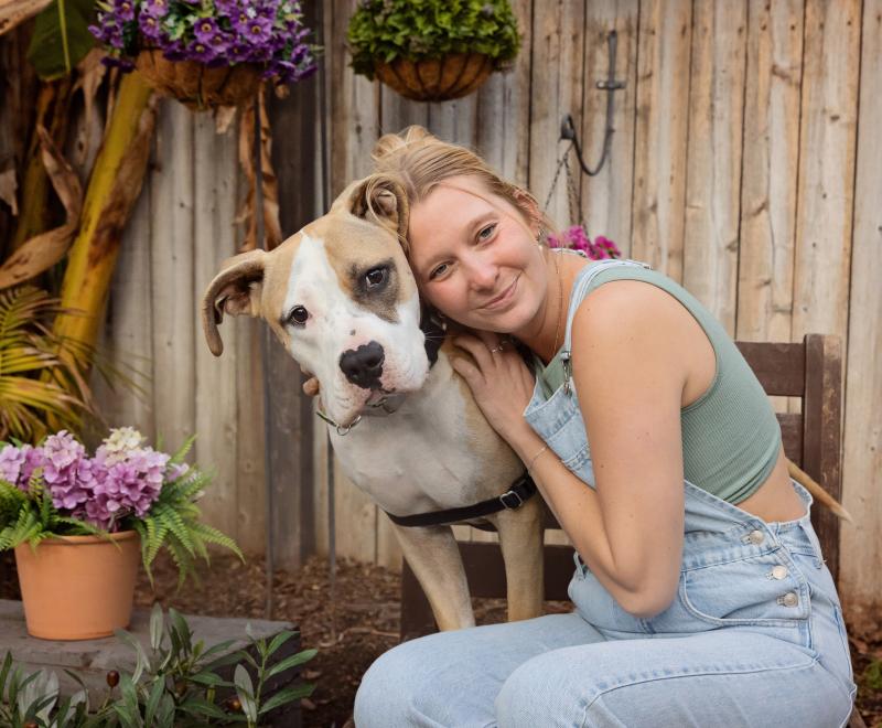 Foster parent hugging large brown and white dog on patio