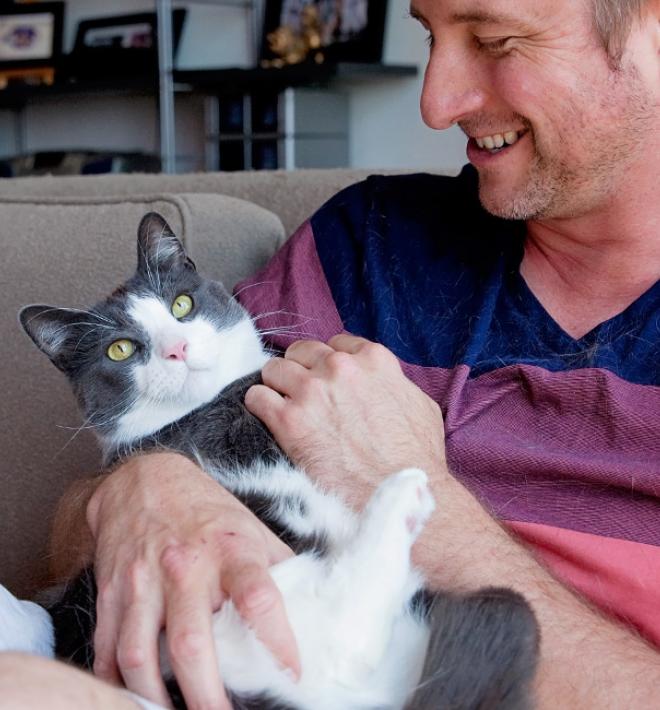 Smiling person relaxing on a couch while holding a cat